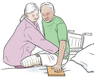 Healthcare provider helping man with amputated leg to use slide board from wheelchair into bed.